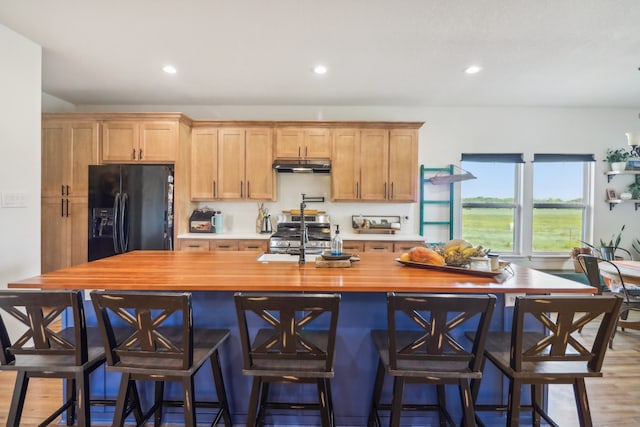 kitchen with wooden counters, hardwood / wood-style floors, black fridge, and a breakfast bar area