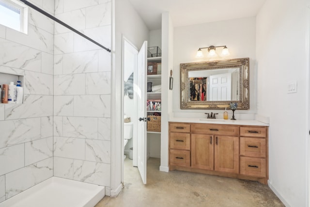 bathroom with vanity, toilet, a tile shower, and concrete flooring