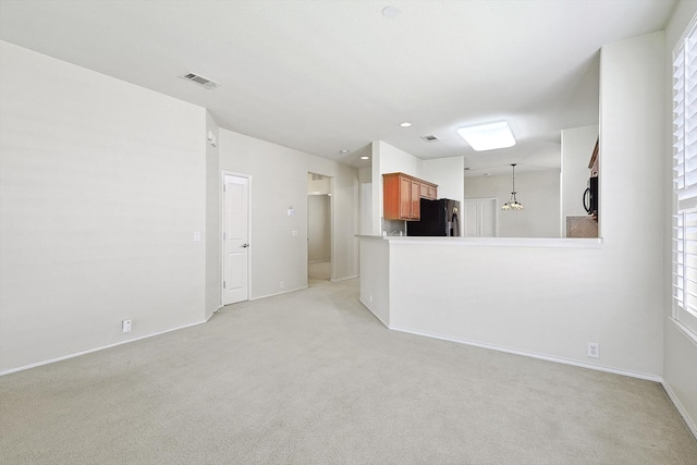 unfurnished living room featuring light colored carpet and a chandelier