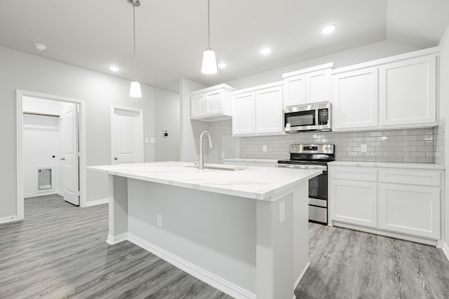 kitchen with tasteful backsplash, decorative light fixtures, a kitchen island with sink, white cabinetry, and appliances with stainless steel finishes