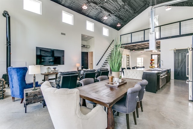 dining area with visible vents, finished concrete flooring, stairway, a barn door, and a towering ceiling