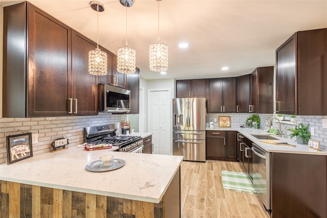 kitchen featuring sink, kitchen peninsula, decorative light fixtures, stainless steel appliances, and light wood-type flooring