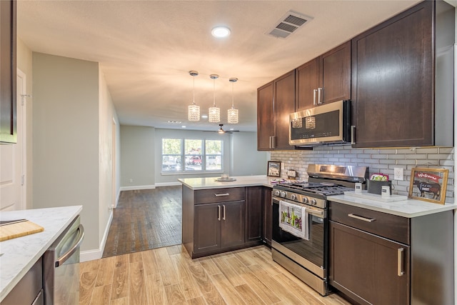 kitchen featuring light wood-type flooring, kitchen peninsula, appliances with stainless steel finishes, decorative light fixtures, and backsplash