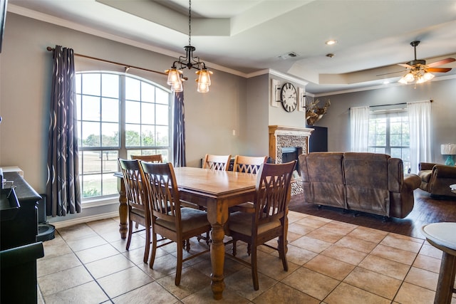 dining space with a stone fireplace, a tray ceiling, crown molding, light hardwood / wood-style floors, and ceiling fan