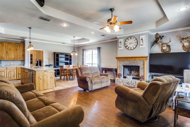 living room with crown molding, a fireplace, a tray ceiling, and light hardwood / wood-style floors