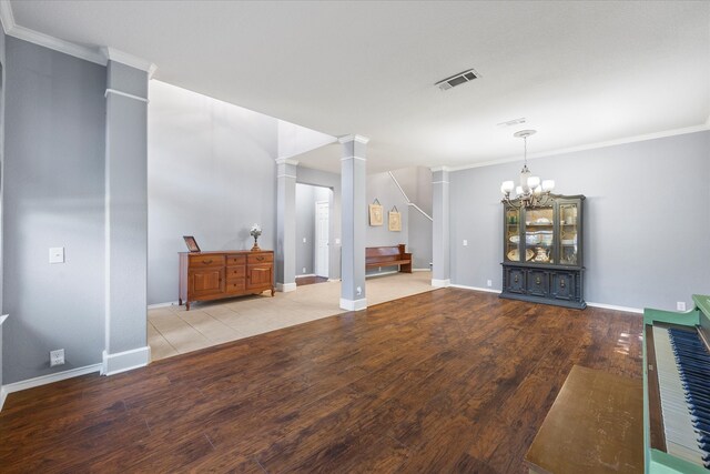 unfurnished living room featuring ornamental molding, light wood-type flooring, decorative columns, and an inviting chandelier