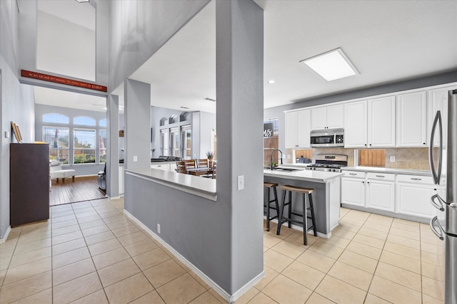 kitchen featuring light tile patterned flooring, a breakfast bar, sink, stainless steel appliances, and white cabinetry