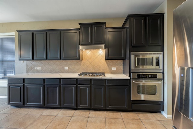 1310 Gold Coast Dr, Rockwall, TX 75087 - kitchen with decorative backsplash, light tile patterned floors, under cabinet range hood, appliances with stainless steel finishes, and light countertops