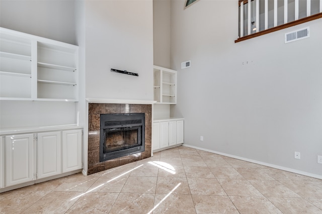 unfurnished living room featuring a tiled fireplace, a towering ceiling, and light tile patterned floors