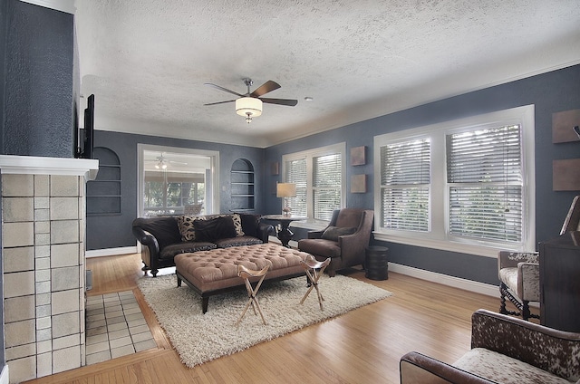 living room with ceiling fan, a textured ceiling, light hardwood / wood-style flooring, and a tiled fireplace