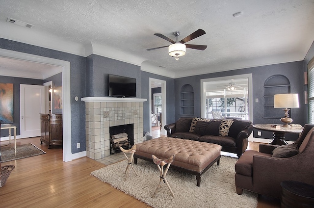 living room featuring light wood-type flooring, ceiling fan, a fireplace, built in shelves, and a textured ceiling