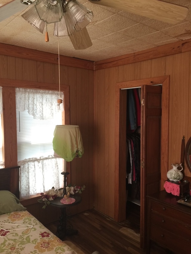 bedroom with dark wood-type flooring, ceiling fan, and wood walls