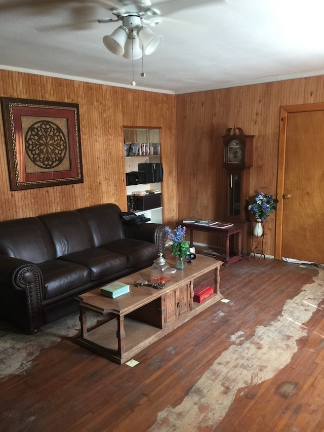 living room with wood walls, dark wood-type flooring, crown molding, and ceiling fan