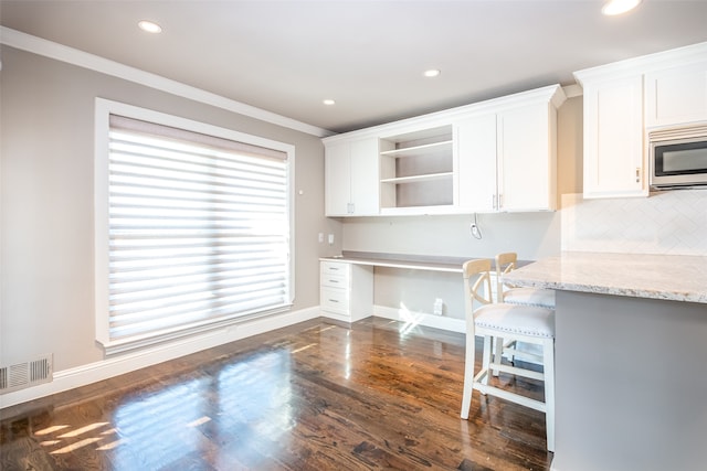 unfurnished office featuring crown molding, built in desk, and dark hardwood / wood-style floors