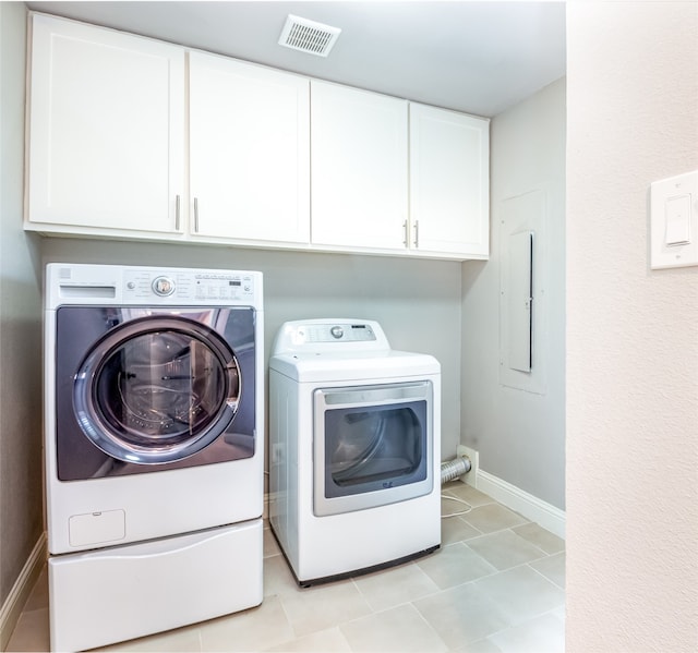 clothes washing area featuring electric panel, washer and dryer, light tile patterned floors, and cabinets