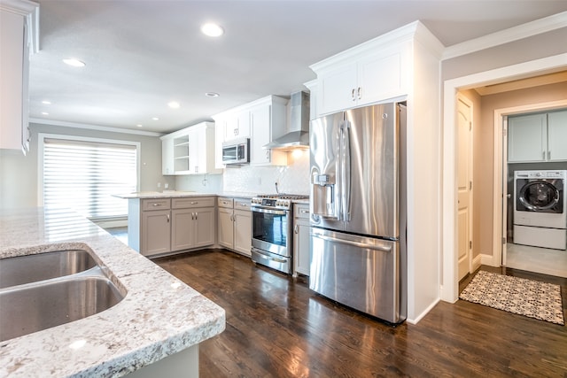 kitchen with wall chimney exhaust hood, white cabinets, appliances with stainless steel finishes, and washer / dryer