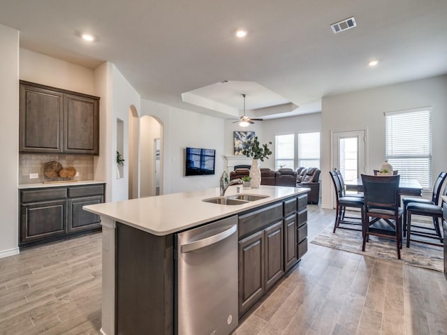 kitchen featuring sink, a raised ceiling, light hardwood / wood-style flooring, stainless steel dishwasher, and a center island with sink