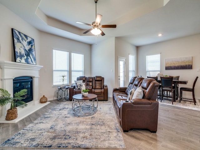 living room with light wood finished floors, a glass covered fireplace, a ceiling fan, and baseboards