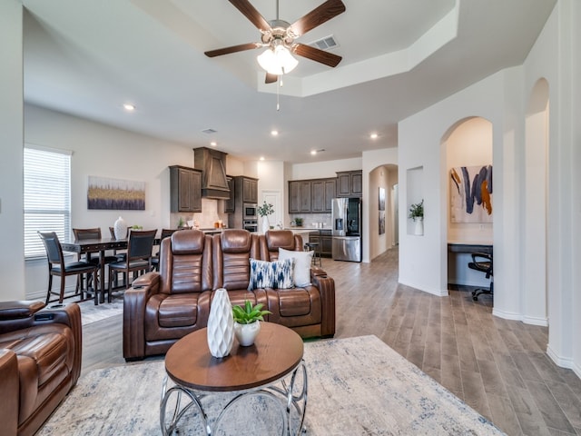 living room with a raised ceiling, ceiling fan, and light hardwood / wood-style floors