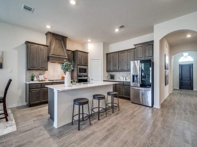 kitchen featuring custom exhaust hood, dark brown cabinets, arched walkways, stainless steel appliances, and visible vents