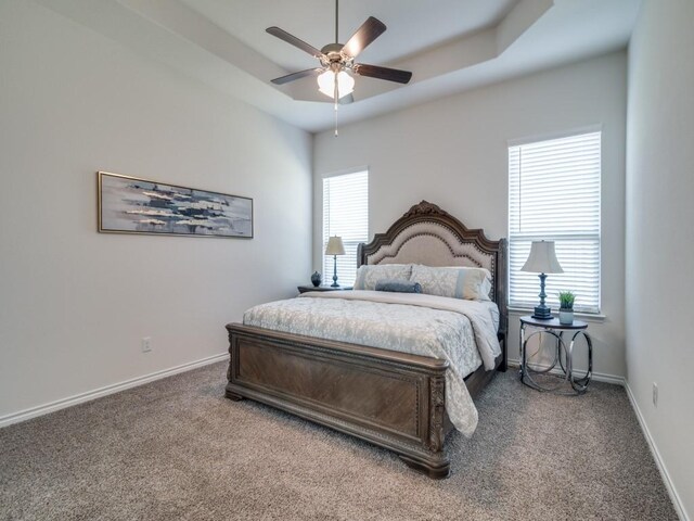 carpeted bedroom with a tray ceiling, ceiling fan, baseboards, and multiple windows