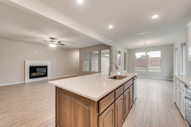 kitchen featuring sink, stainless steel dishwasher, decorative light fixtures, a center island with sink, and ceiling fan with notable chandelier