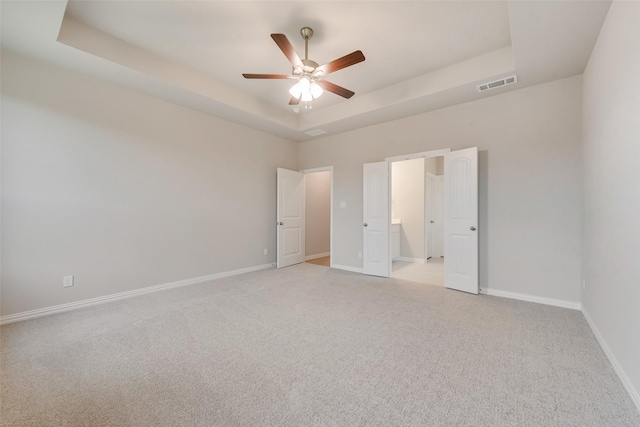 unfurnished bedroom featuring ceiling fan, light carpet, and a tray ceiling