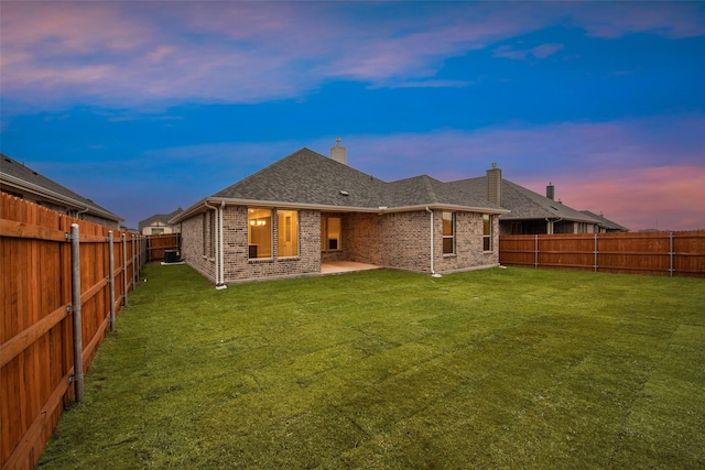 back house at dusk with a patio and a lawn