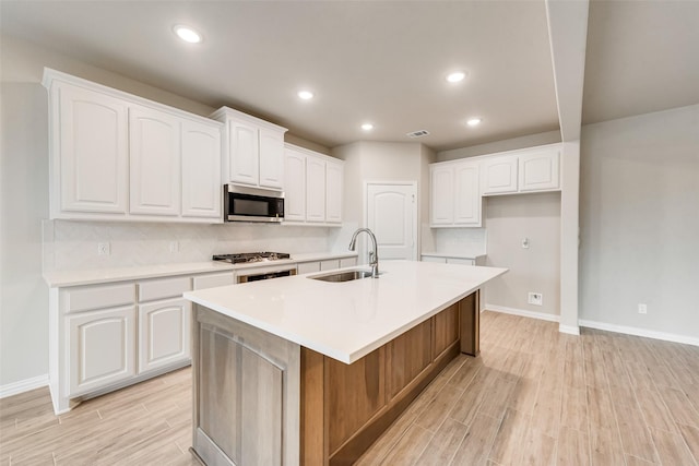 kitchen featuring white cabinets, sink, an island with sink, tasteful backsplash, and stainless steel appliances