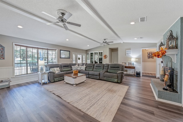 living room featuring ceiling fan, vaulted ceiling with beams, a brick fireplace, a textured ceiling, and dark hardwood / wood-style floors