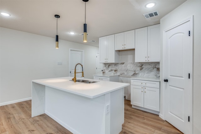 kitchen featuring white cabinetry, sink, tasteful backsplash, pendant lighting, and a center island with sink