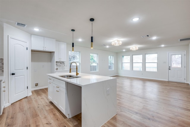 kitchen with sink, tasteful backsplash, decorative light fixtures, a center island with sink, and white cabinets