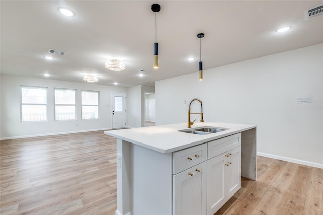 kitchen with white cabinetry, sink, light hardwood / wood-style flooring, decorative light fixtures, and a kitchen island with sink