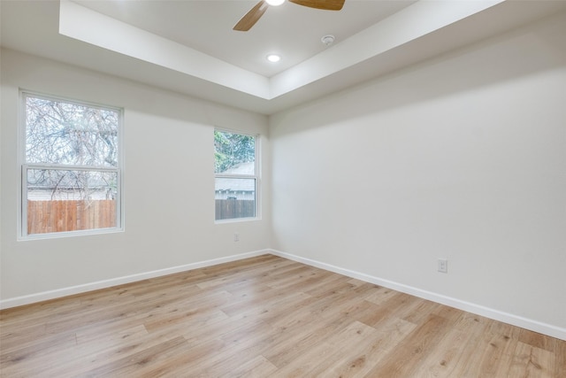 empty room with ceiling fan, a tray ceiling, and light hardwood / wood-style flooring