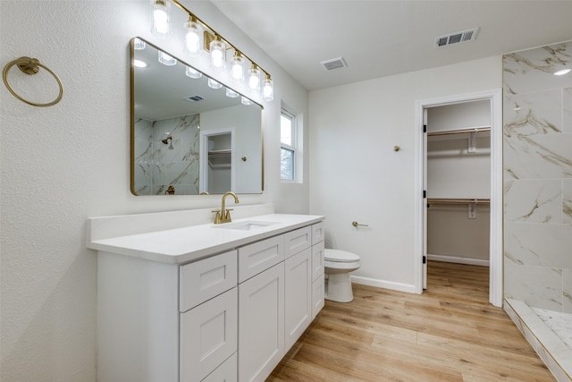 bathroom featuring a tile shower, vanity, wood-type flooring, and toilet