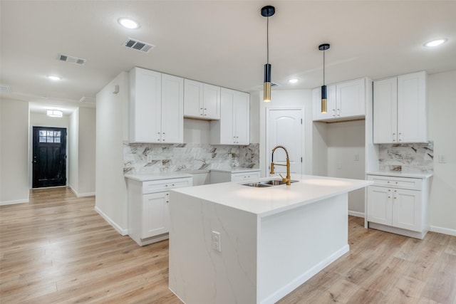 kitchen featuring tasteful backsplash, sink, pendant lighting, white cabinetry, and an island with sink