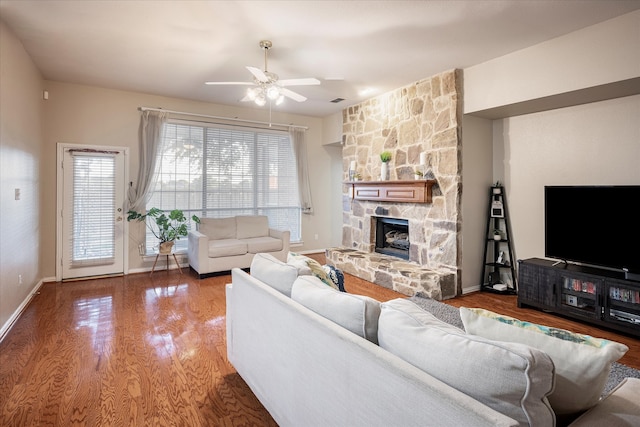 living room with a stone fireplace, wood-type flooring, and ceiling fan