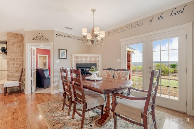 dining space with a tile fireplace, french doors, ornamental molding, a notable chandelier, and light hardwood / wood-style floors