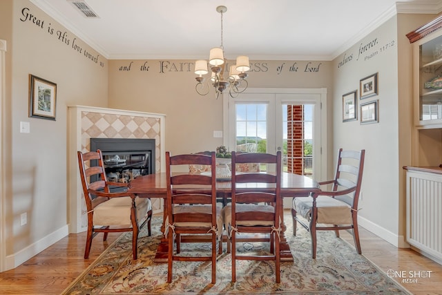 dining room featuring a notable chandelier, light wood-type flooring, ornamental molding, and a tile fireplace