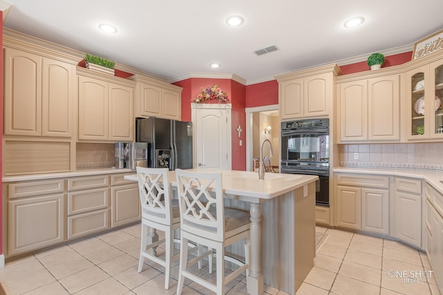 kitchen with tasteful backsplash, a kitchen island with sink, black appliances, light tile patterned floors, and a breakfast bar area