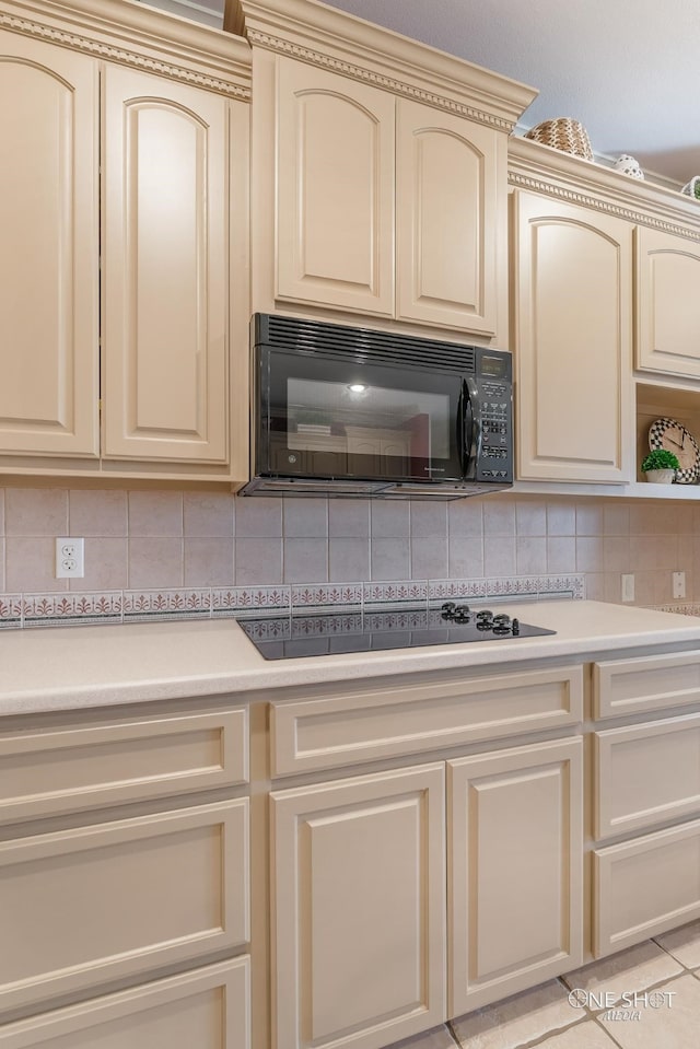 kitchen with cream cabinetry, light tile patterned floors, tasteful backsplash, and black appliances