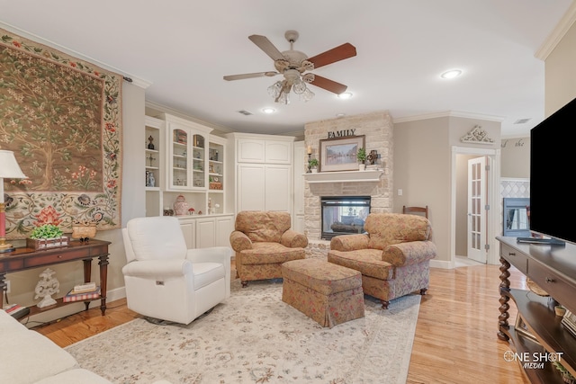 living room with ceiling fan, ornamental molding, a fireplace, and light hardwood / wood-style flooring