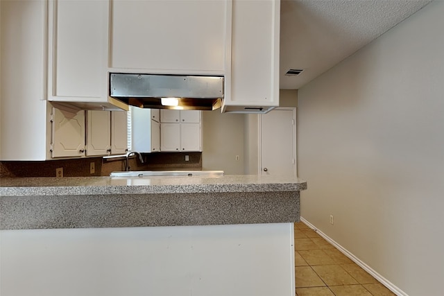 kitchen featuring extractor fan, white cabinets, light tile patterned floors, and a textured ceiling