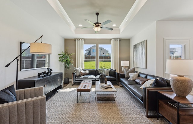 carpeted living room with ceiling fan and a raised ceiling