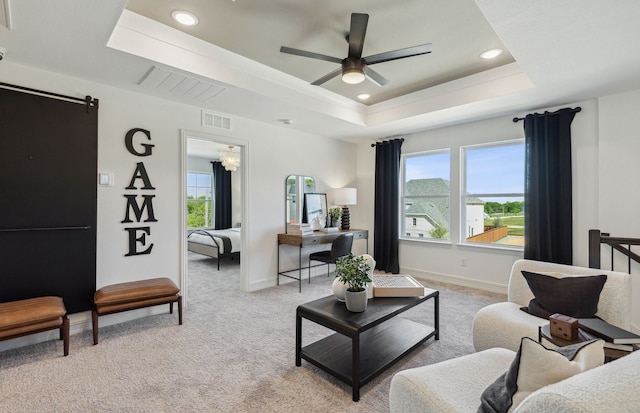 living room featuring ceiling fan with notable chandelier, light colored carpet, and a tray ceiling