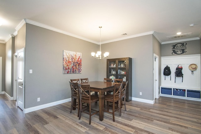 dining room featuring visible vents, ornamental molding, wood finished floors, a chandelier, and baseboards