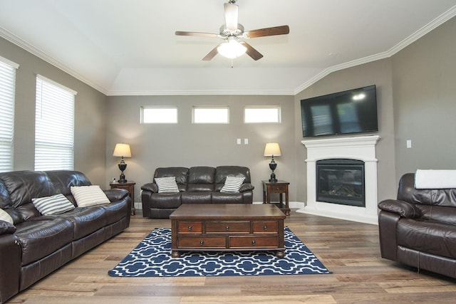 living area featuring lofted ceiling, wood finished floors, a ceiling fan, ornamental molding, and a glass covered fireplace