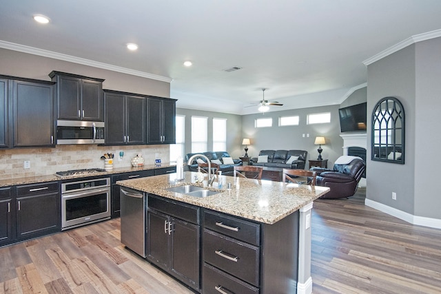 kitchen with an island with sink, hardwood / wood-style floors, sink, crown molding, and appliances with stainless steel finishes