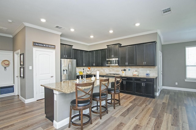 kitchen featuring light stone counters, visible vents, appliances with stainless steel finishes, an island with sink, and a kitchen breakfast bar