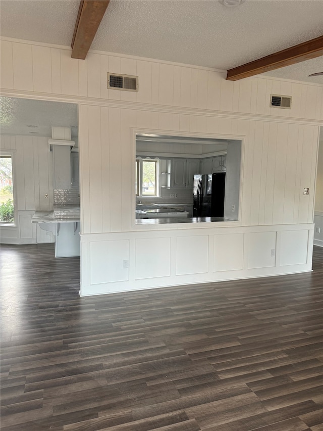 unfurnished living room featuring a textured ceiling, beamed ceiling, and dark wood-type flooring